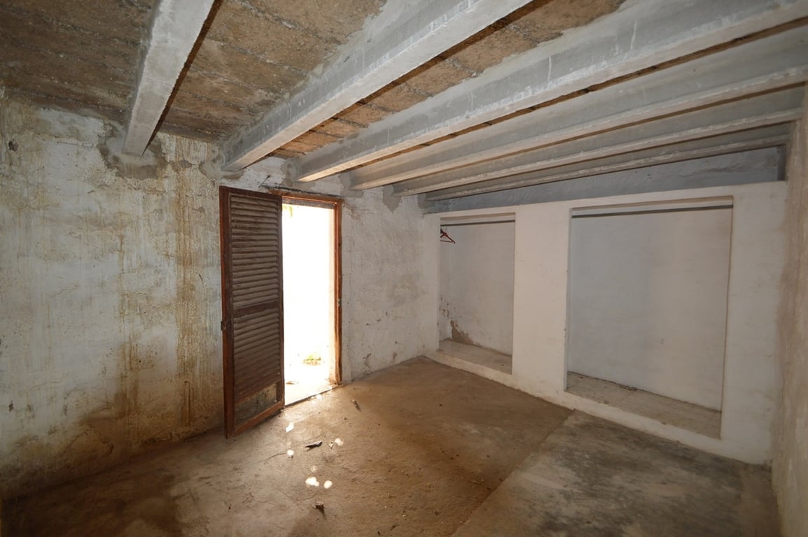Grand espace de rangement avec poutres apparentes, niches murales intégrées et porte persienne en bois offrant un accès direct vers l'extérieur.