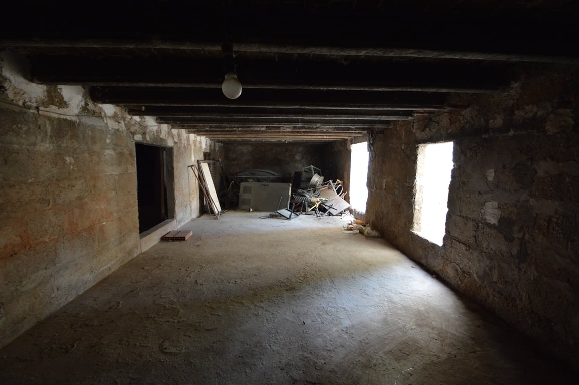 Grand espace ouvert avec poutres en bois apparentes et murs en pierre, offrant un potentiel de rénovation pour un studio ou une zone de stockage.
