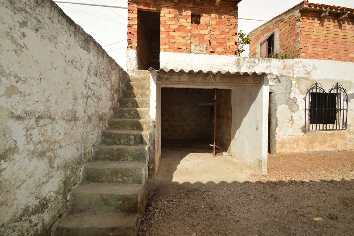 Patio extérieur avec escalier en béton, espace de rangement couvert et murs en briques apparentes à rénover dans le centre historique.