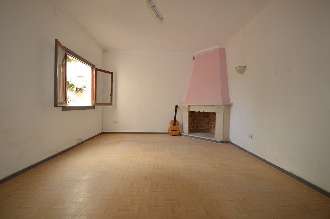 Pièce spacieuse avec cheminée d'angle rose, parquet au sol et fenêtre en bois offrant une vue sur la végétation extérieure.