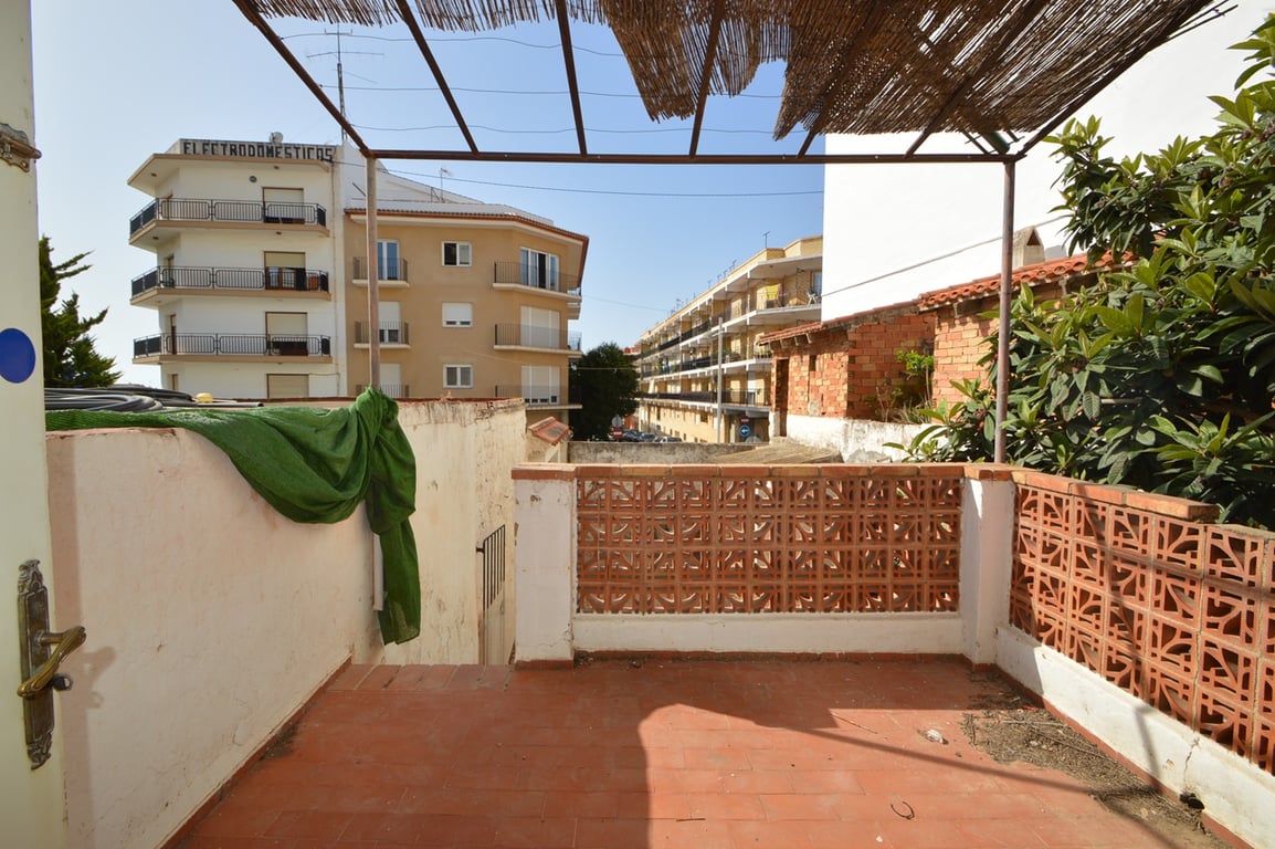 Terrasse extérieure avec sol en terre cuite et garde-corps en briques ajourées, abritée par une pergola métallique avec couverture en canisse.