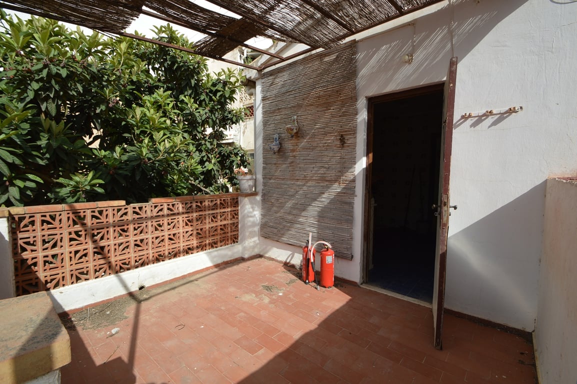 Terrasse extérieure avec sol en terre cuite, pergola en canisse et muret décoratif en briques ajourées bordé de végétation.