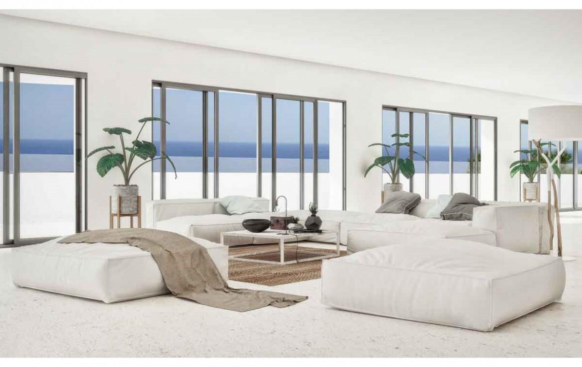 Salon minimaliste avec canapés modulables blancs, sol en pierre claire et grandes baies vitrées offrant une vue panoramique sur la mer Méditerranée.