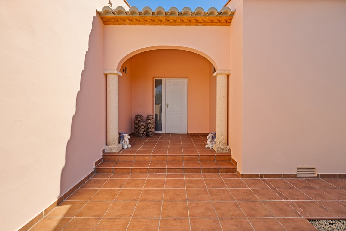Entrée principale avec porche voûté, colonnes en pierre de Tosca et sol en terre cuite. La façade aux tons chauds et les marches d'accès soulignent le style méditerranéen.