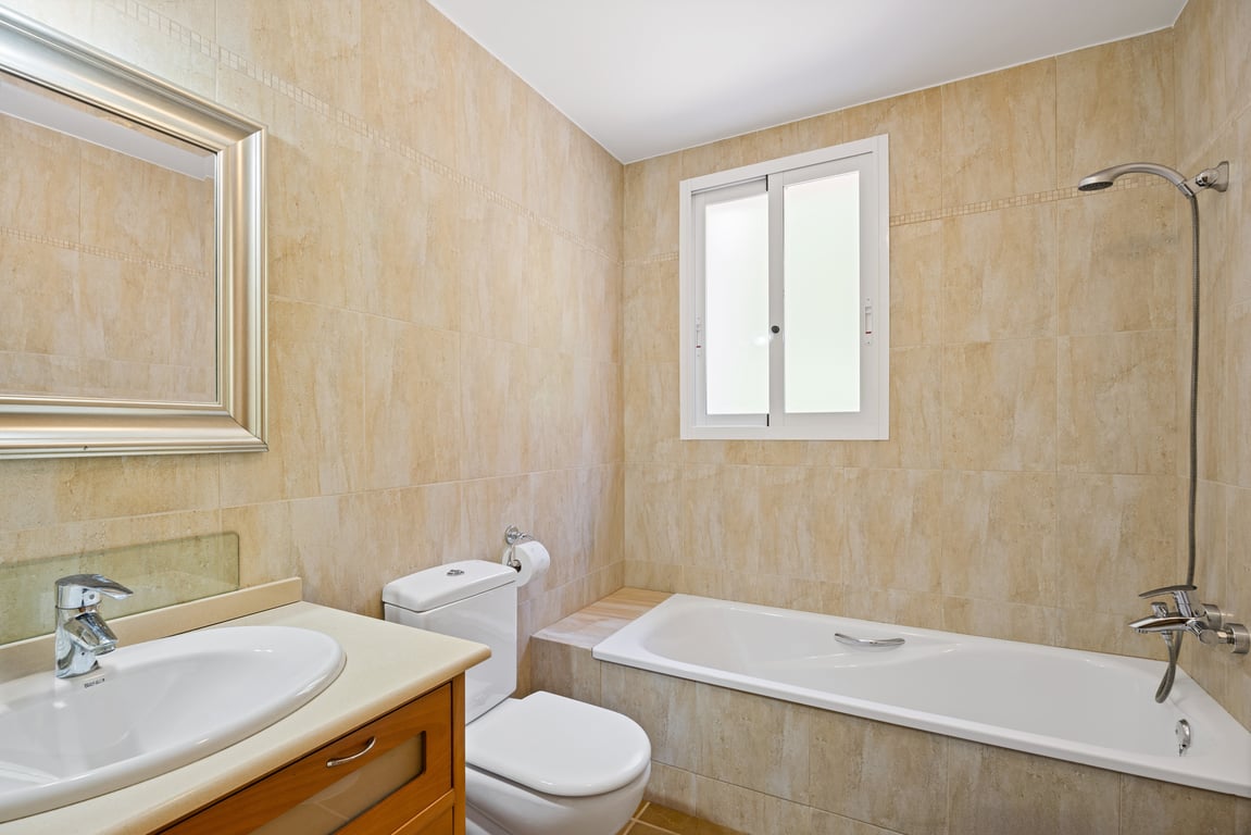Salle de bain fonctionnelle avec carrelage beige, baignoire intégrée, meuble vasque en bois et fenêtre en verre dépoli apportant une luminosité naturelle.