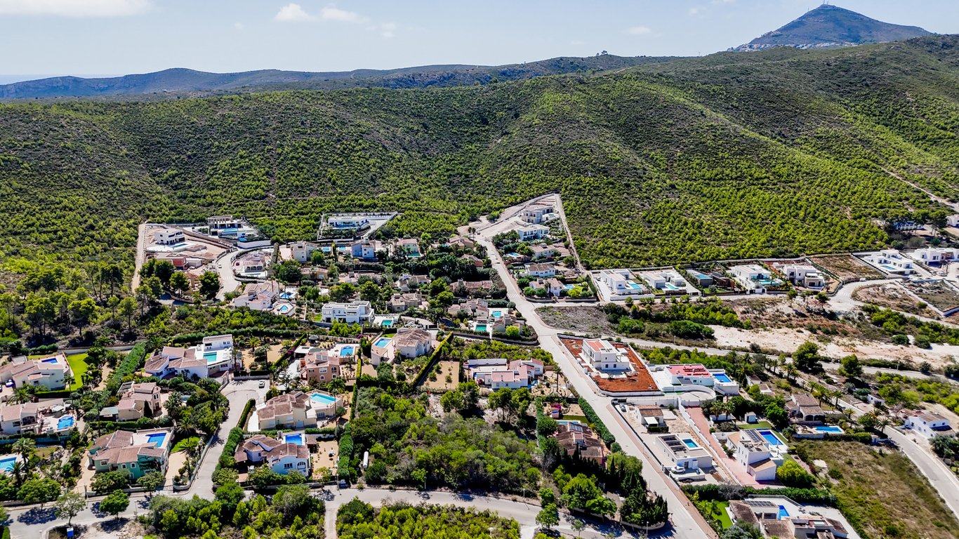 Vue aérienne de l'urbanisation à Jávea, illustrant l'emplacement calme de la villa au pied des collines verdoyantes et de la nature.