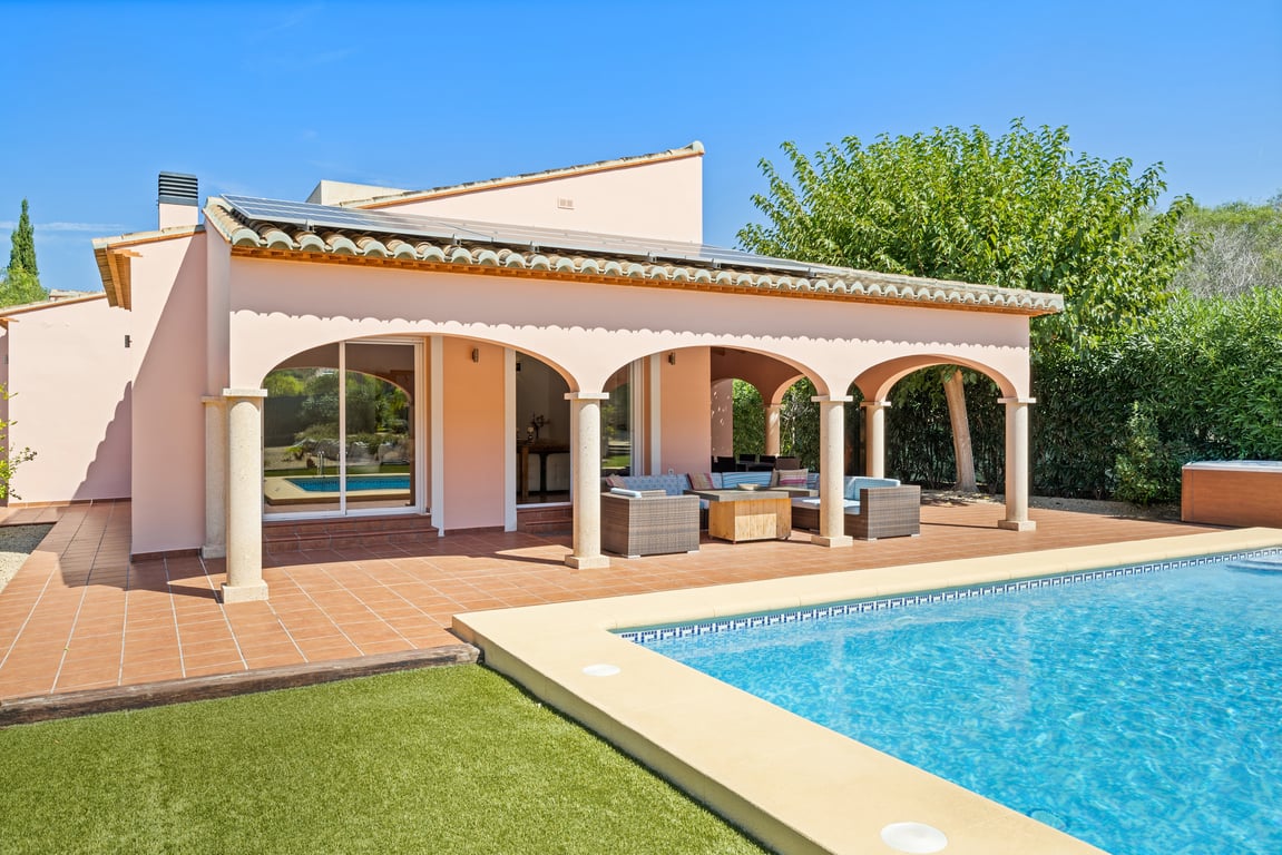 Vue extérieure avec piscine, naya couverte aux arches élégantes et colonnes en pierre, et panneaux solaires installés sur la toiture traditionnelle.