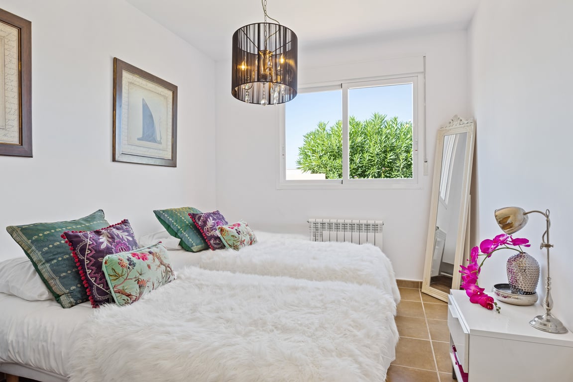 Chambre avec lits jumeaux, couvre-lits blancs duveteux, lustre noir à cristaux et fenêtre coulissante offrant une vue sur le jardin.
