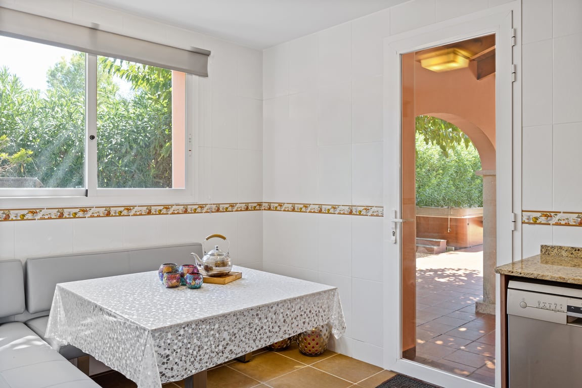 Coin petit-déjeuner dans la cuisine avec banquette intégrée, murs carrelés et porte vitrée offrant un accès direct à la terrasse couverte.