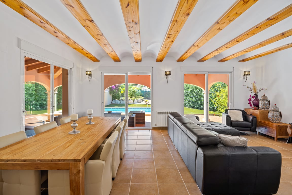 Salon-salle à manger lumineux avec poutres apparentes en bois, sol en terre cuite et grandes baies vitrées offrant un accès direct à la terrasse et à la piscine.