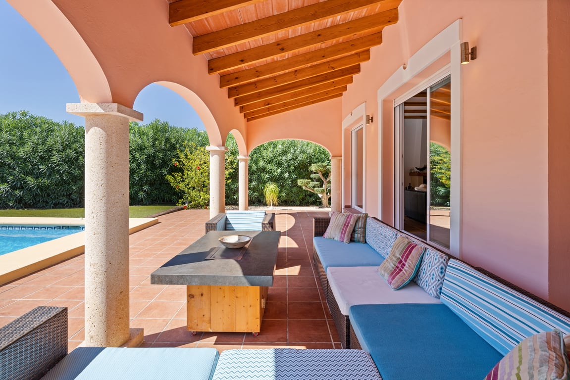 Terrasse couverte avec poutres en bois, colonnes en pierre naturelle et salon d'été donnant sur la piscine et les espaces verts.