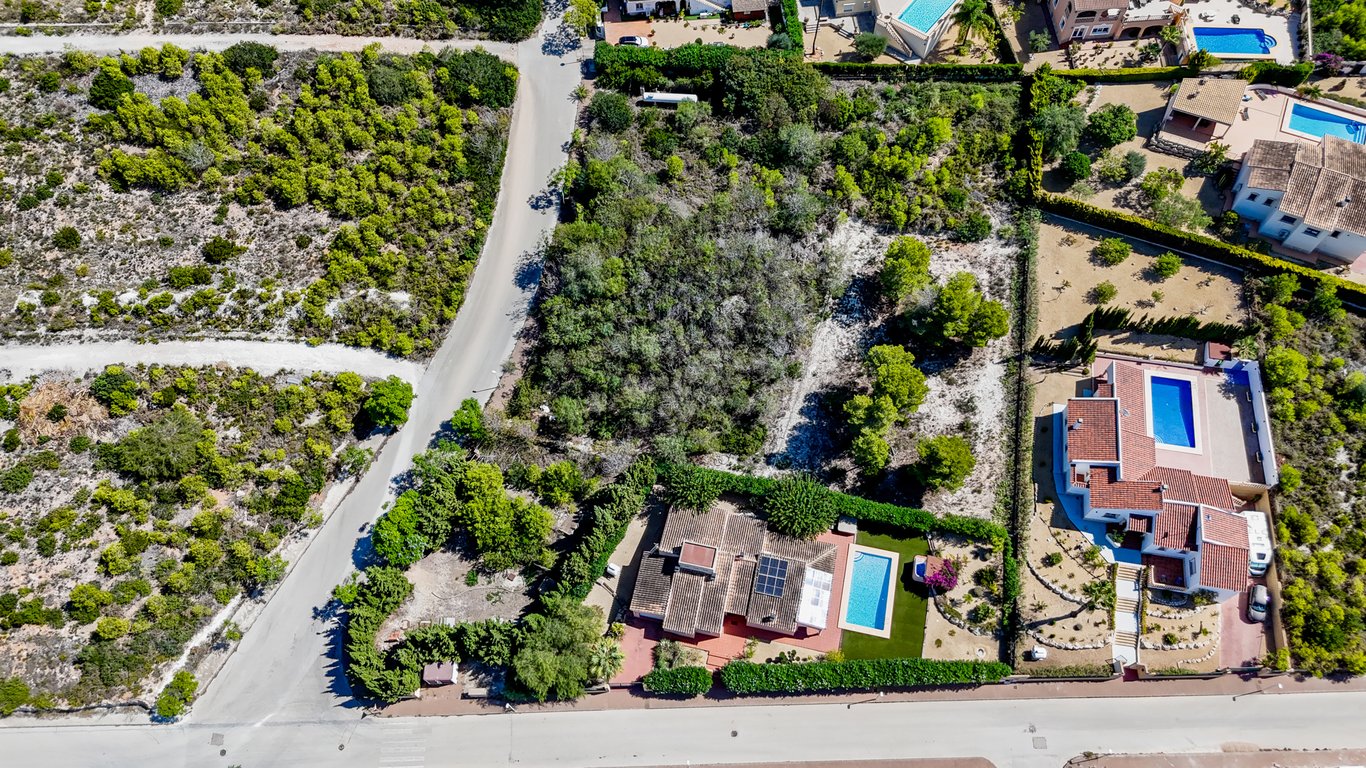 Vue aérienne de la villa avec panneaux solaires et piscine, ainsi que le vaste terrain urbain adjacent arboré situé à Jávea.