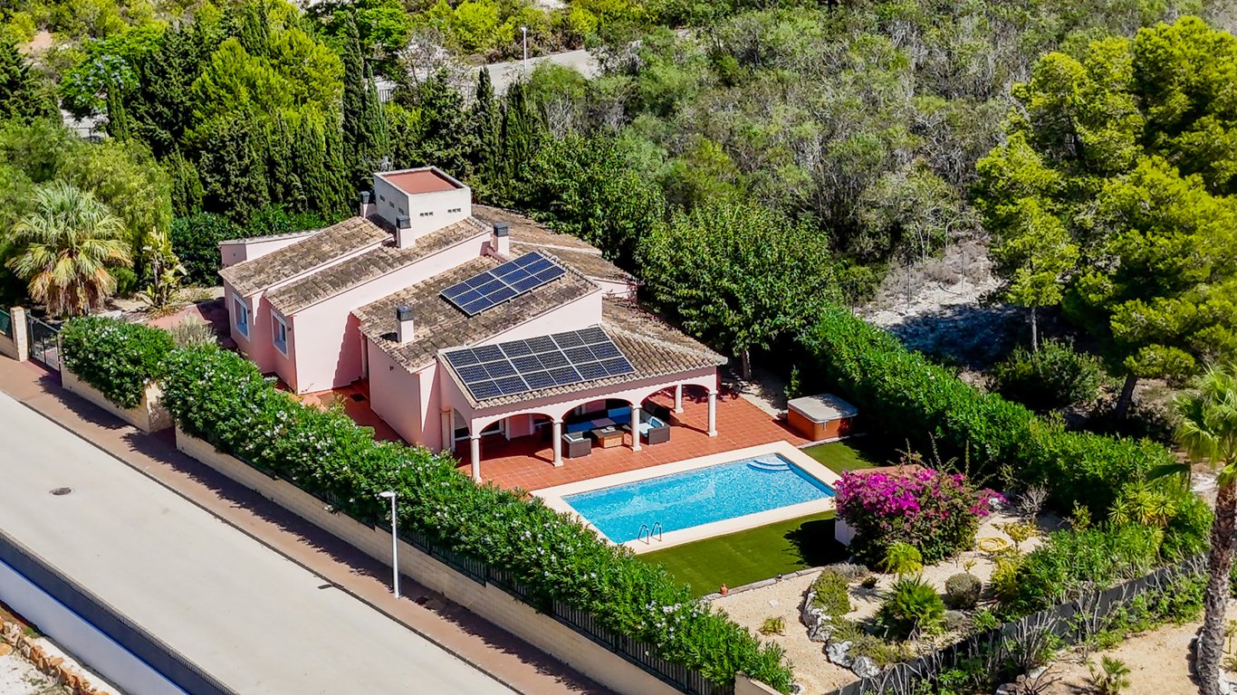Vue aérienne de la villa avec panneaux solaires, naya couverte face à la piscine et jardin méditerranéen aménagé avec jacuzzi.