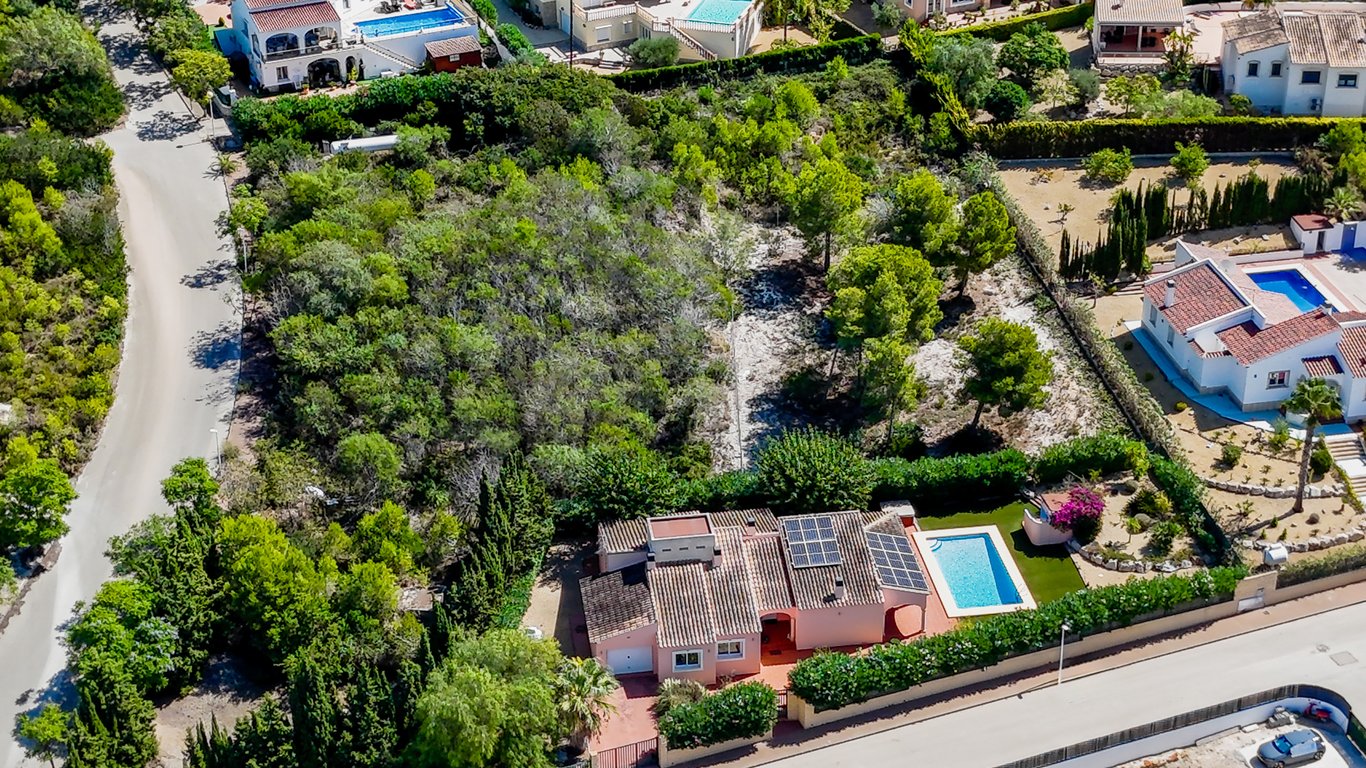 Vue aérienne de la villa avec panneaux solaires, piscine et le terrain constructible attenant arboré au cœur d'un quartier résidentiel calme.