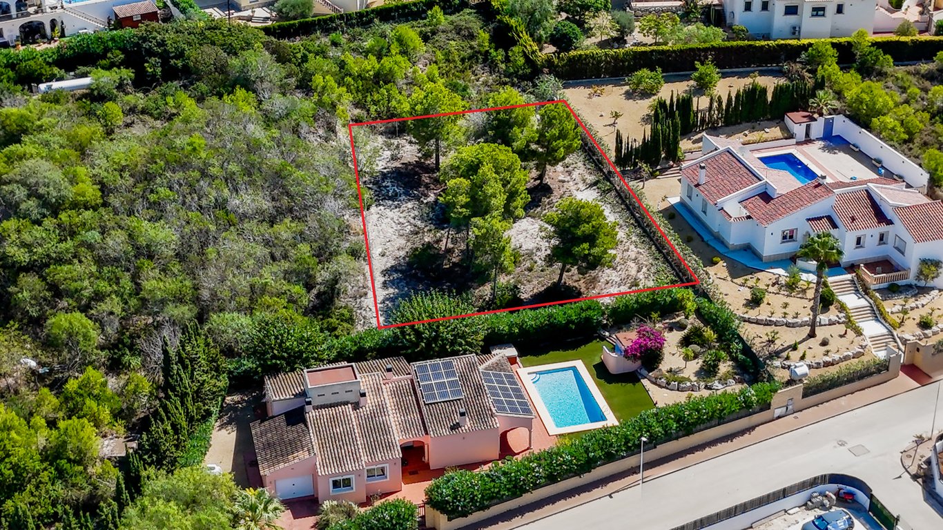 Vue aérienne montrant la villa avec panneaux solaires et piscine, ainsi que le terrain urbain adjacent avec des pins matures, délimité en rouge.