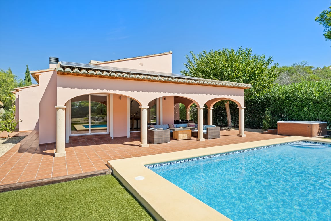 Vue extérieure de la villa avec naya à arcades, piliers en pierre, terrasse en terre cuite, piscine en mosaïque, panneaux solaires et jacuzzi extérieur.