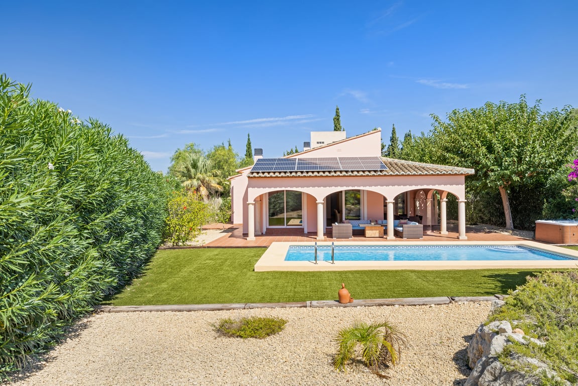 Vue extérieure de la villa avec piscine, naya couverte à arches, panneaux solaires et jardin facile d'entretien composé de gazon synthétique et gravier.