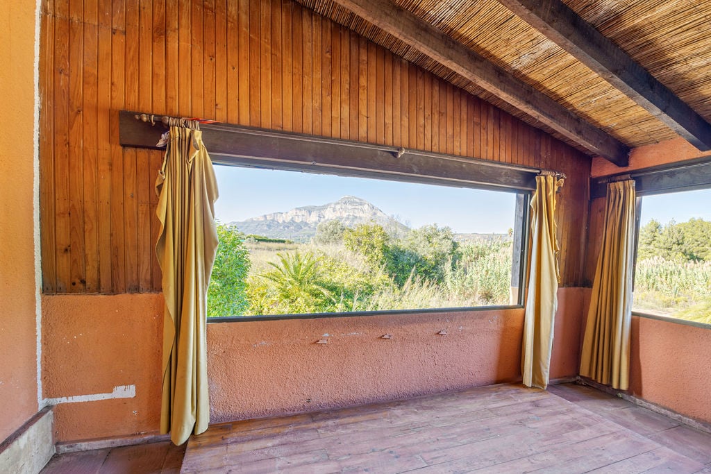 Espace intérieur avec plafonds en bois et canisse, offrant une vue cadrée sur le massif du Montgó à travers une large fenêtre panoramique.