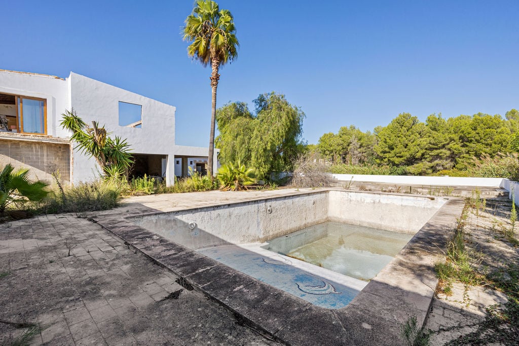 Grande piscine extérieure avec mosaïques et vaste terrasse, entourée d'une végétation méditerranéenne et d'un bâtiment blanc au style contemporain.