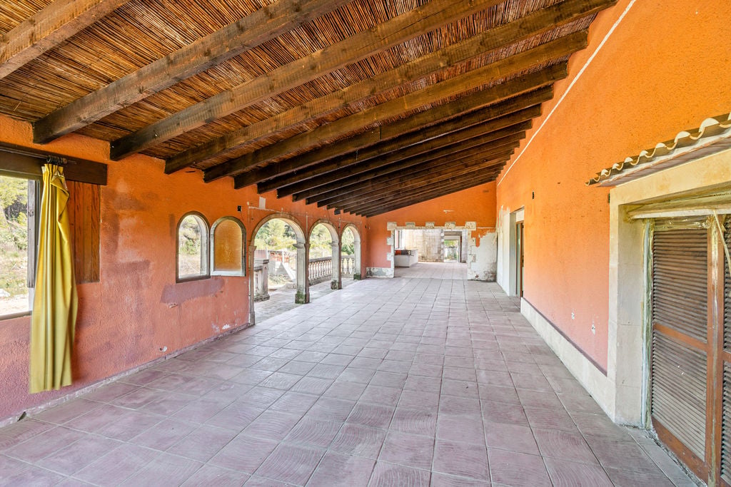 Grande terrasse couverte avec plafond en poutres de bois et canisse, murs terracotta et arches en pierre s'ouvrant sur l'extérieur.