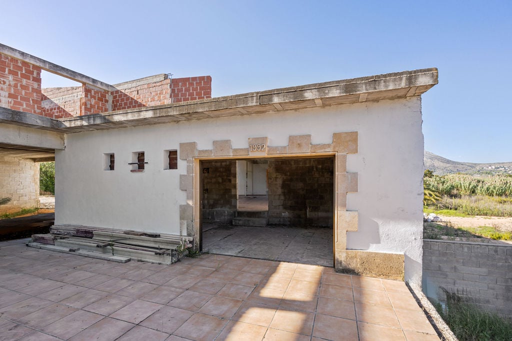 Structure en rénovation avec terrasse carrelée, encadrements en pierre traditionnelle et inscription de l'année 1992 au-dessus de l'entrée.