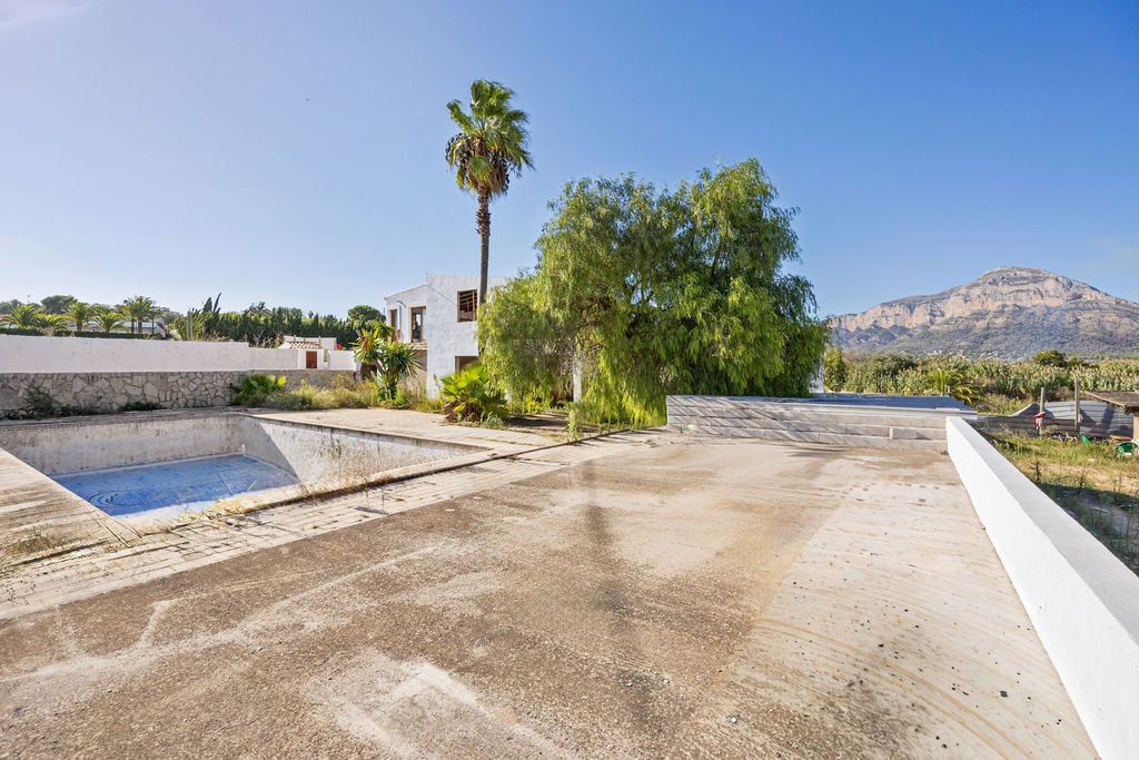Terrasse extérieure en béton avec vue panoramique sur le Montgó, comprenant une piscine à rénover et un bâtiment de style méditerranéen.