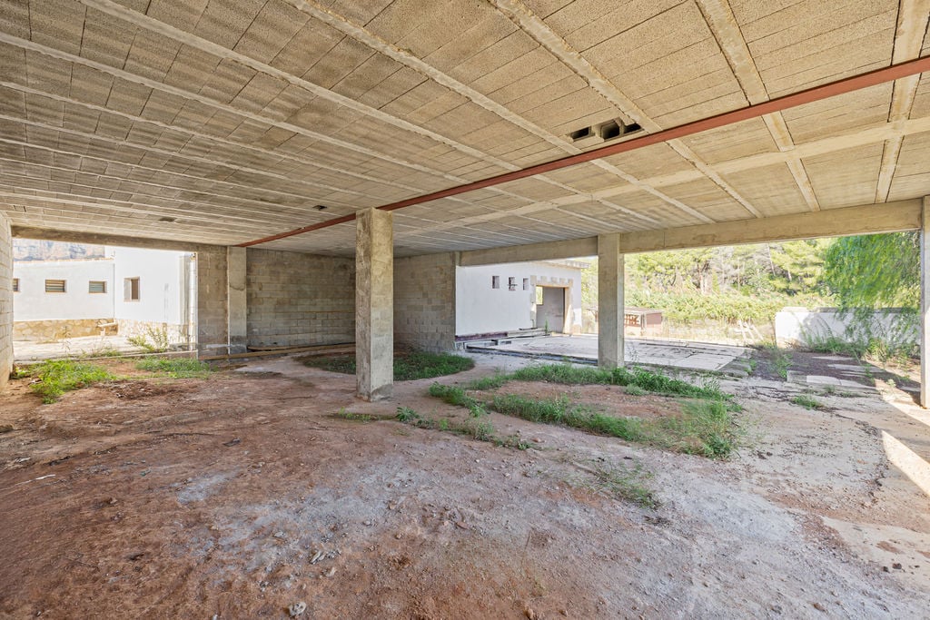 Vaste espace brut à plan ouvert avec piliers en béton et plafonds à poutrelles, offrant une base structurelle solide pour un aménagement sur mesure.