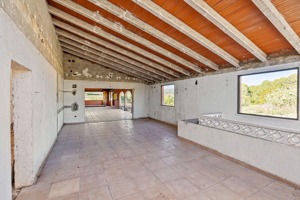 Vaste espace intérieur ouvert avec hauts plafonds inclinés, poutres en béton apparentes et carrelage au sol. Grandes ouvertures offrant une vue sur la végétation.