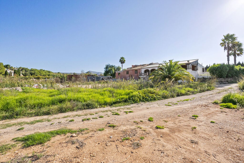 Vue extérieure du vaste terrain rustique comprenant une bâtisse méditerranéenne traditionnelle avec des arches et des palmiers sous le soleil de Jávea.