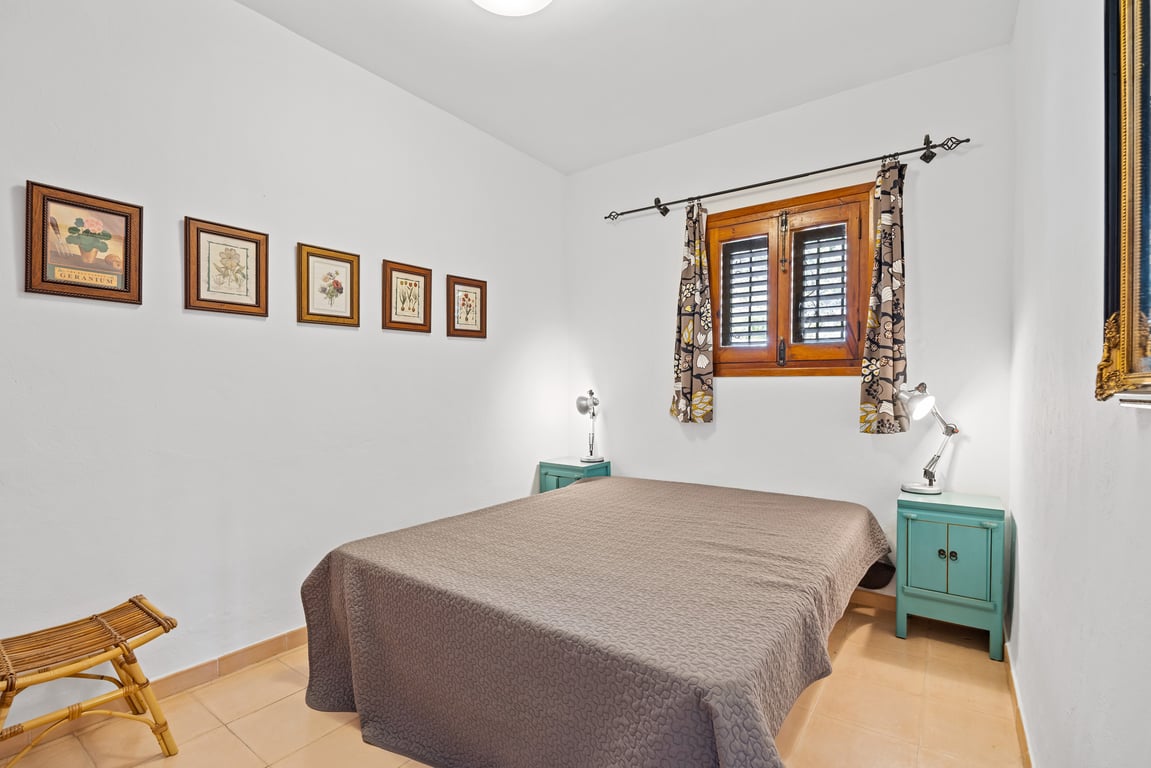 Chambre avec lit double, tables de chevet turquoise et fenêtre en bois avec volets traditionnels. Les murs blancs sont ornés d'une série de cadres botaniques.