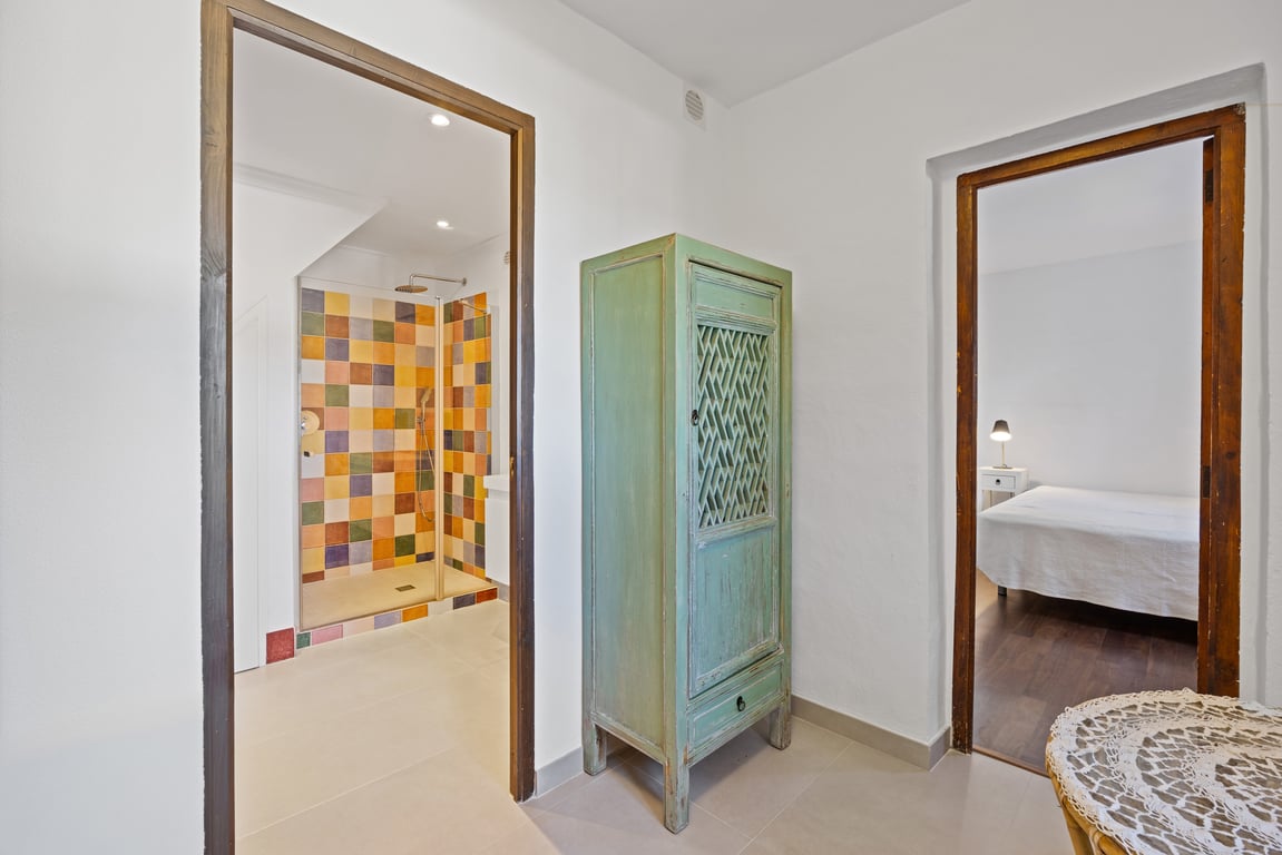 Couloir de distribution avec armoire rustique verte, menant à une chambre et une salle de bain moderne aux carreaux colorés.