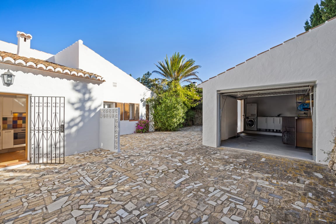 Cour extérieure pavée de pierres avec accès à la cuisine et un garage indépendant comprenant un espace buanderie aménagé.