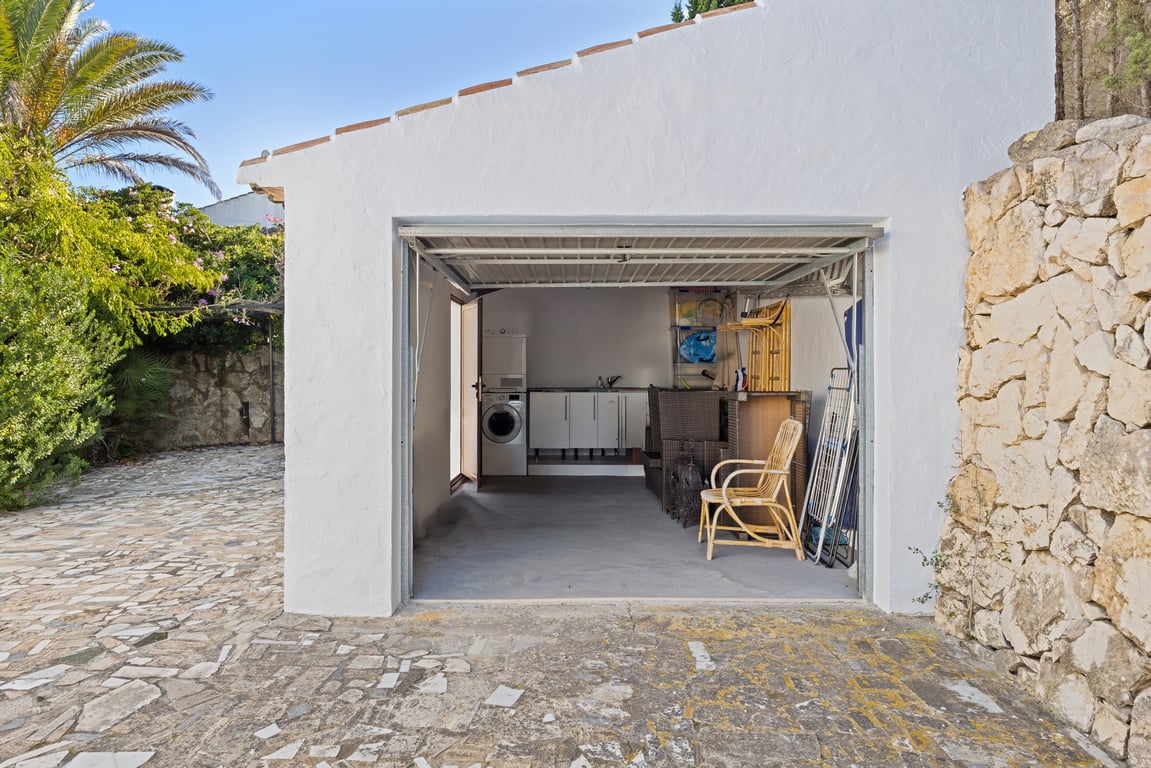 Garage fonctionnel avec espace buanderie équipé d'un lave-linge, d'un sèche-linge et de rangements, situé à côté d'un mur en pierre naturelle et d'une allée pavée.