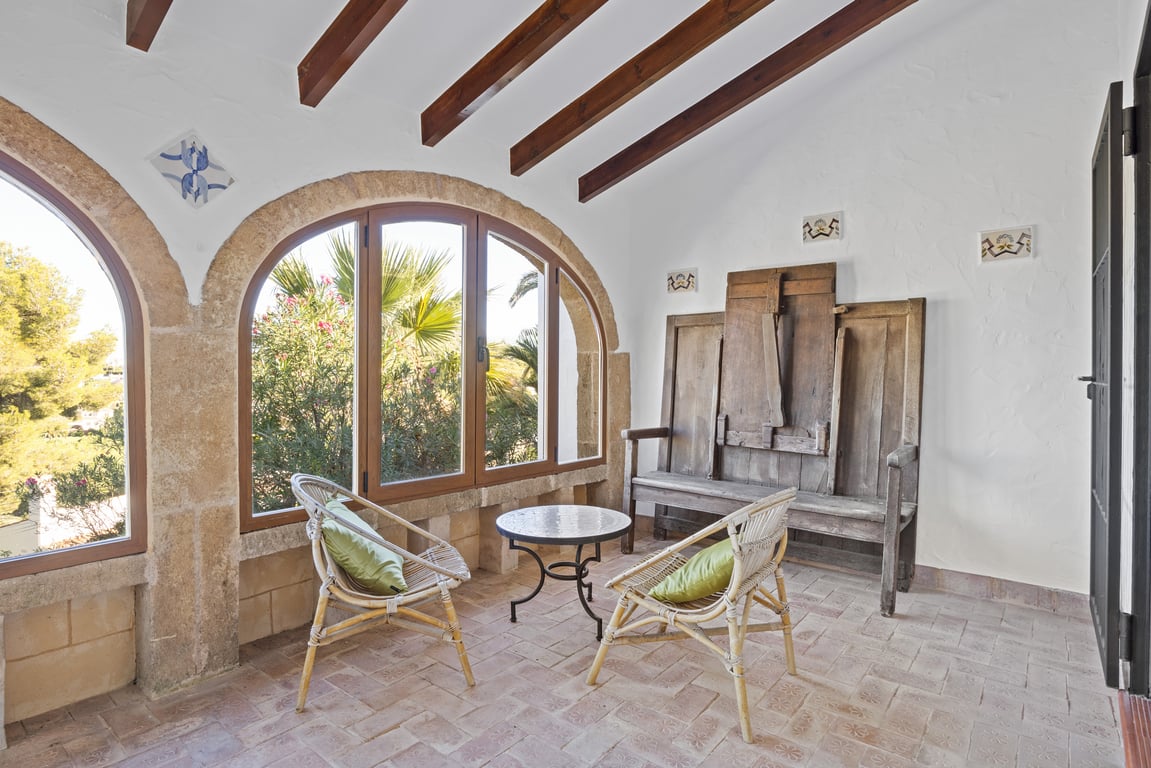 Naya vitrée avec arches en pierre Tosca, poutres apparentes et sol en terre cuite. Cet espace de vie traditionnel offre un mobilier rustique et une vue sur le jardin.