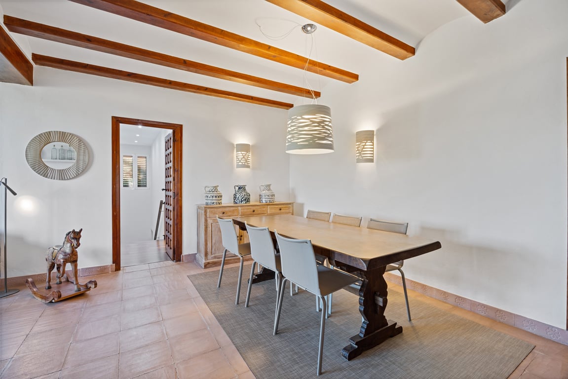 Salle à manger avec poutres en bois apparentes, sol en terre cuite artisanale et table massive, éclairée par des luminaires au design moderne.