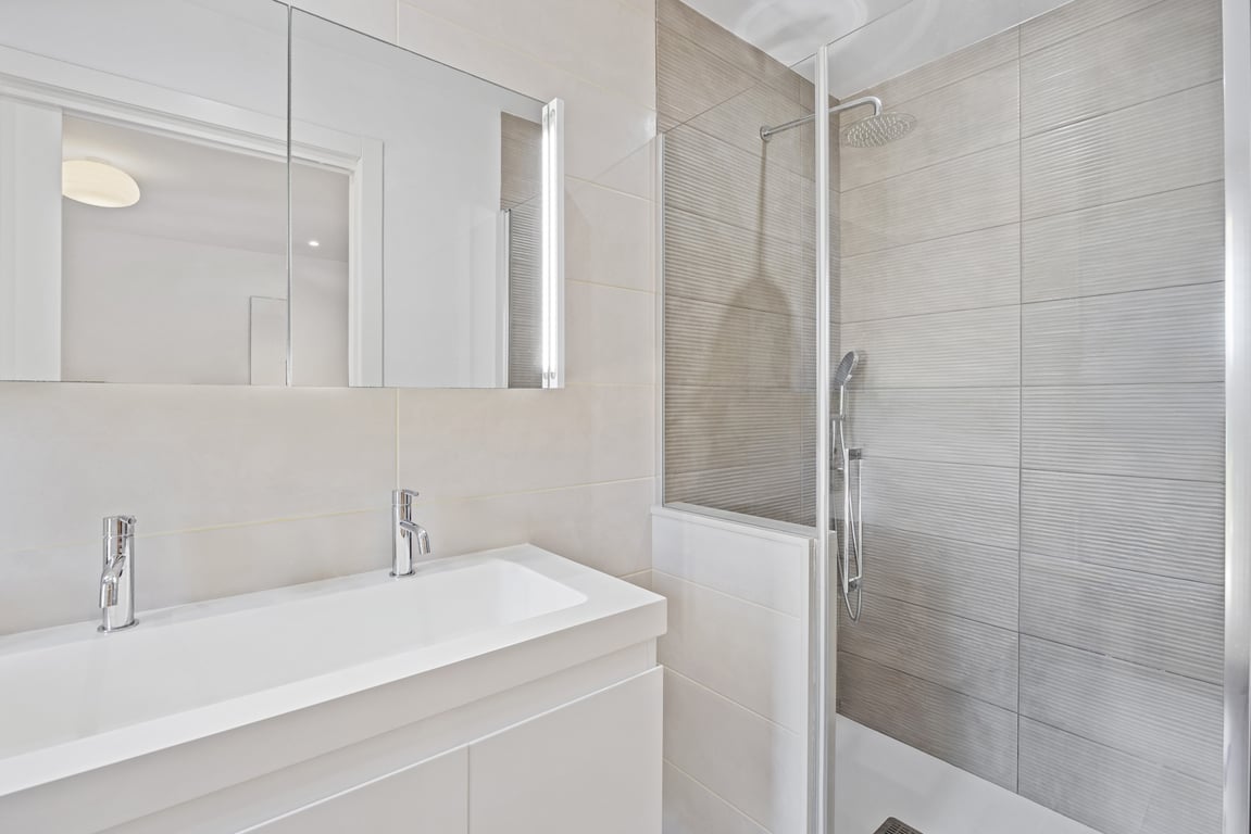 Salle de bains moderne rénovée avec double vasque, armoire de toilette éclairée et douche à l'italienne avec carrelage texturé et paroi vitrée.