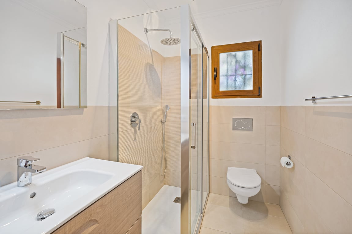 Salle de bains moderne rénovée avec douche à l'italienne vitrée, meuble vasque en bois clair et carrelage élégant dans des tons beige.