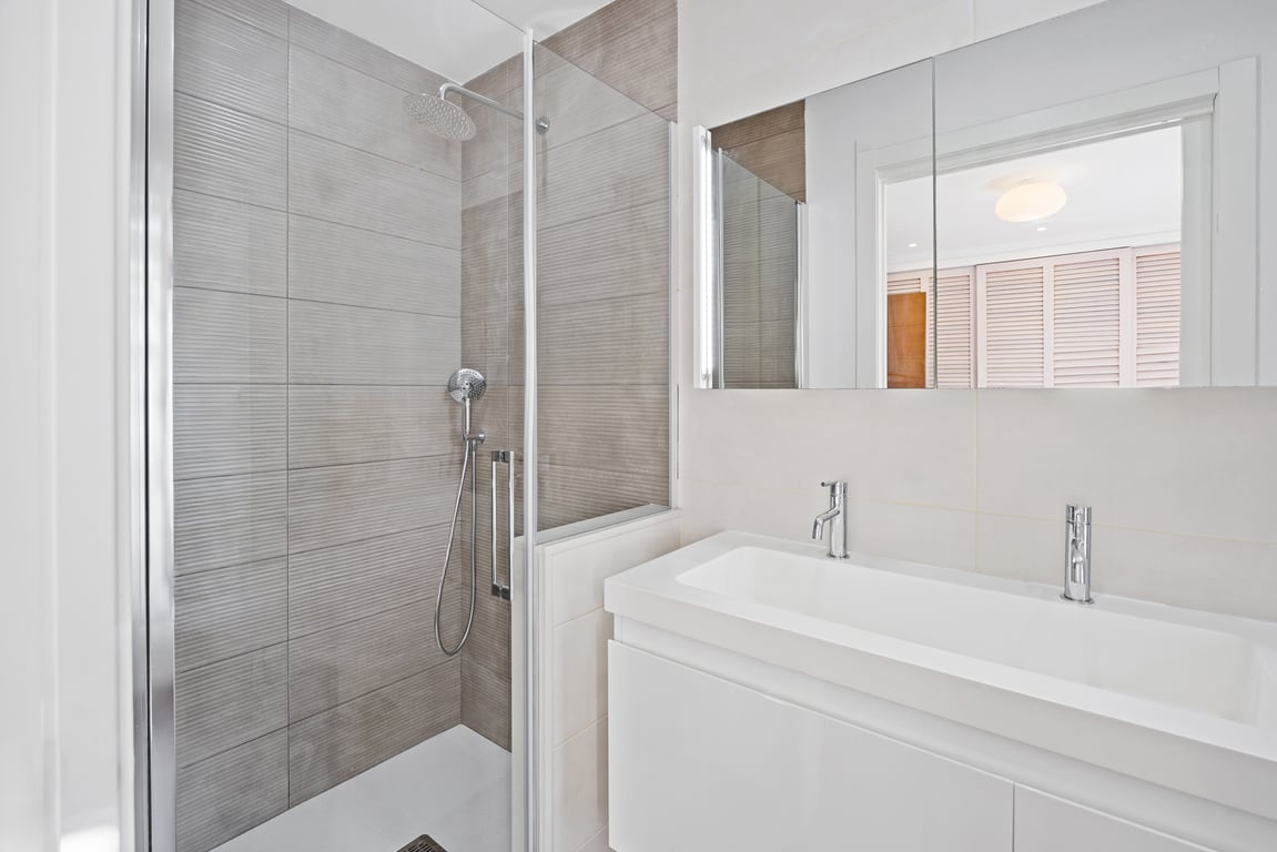 Salle d'eau moderne avec douche à l'italienne en carreaux gris texturés, paroi en verre et meuble vasque blanc épuré avec robinetterie chromée.