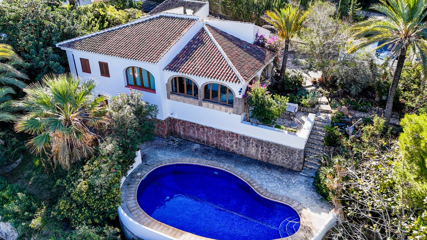 Vue aérienne de la villa avec piscine en forme de rein, façade blanche sur socle en pierre et naya vitrée aux arches en pierre de Tosca authentique.