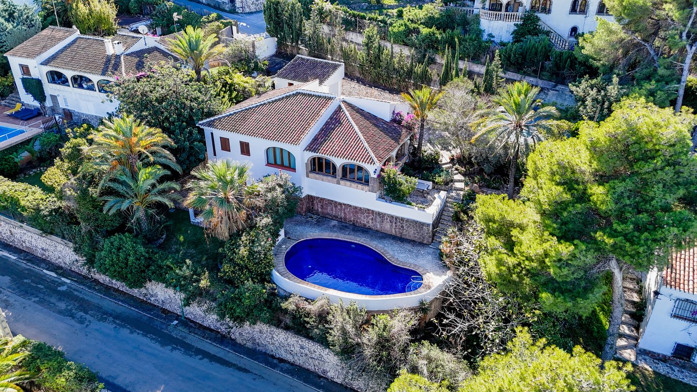 Vue aérienne de la villa traditionnelle avec piscine en forme de rein, toiture en terre cuite et naya voûtée, entourée d'un jardin méditerranéen luxuriant.
