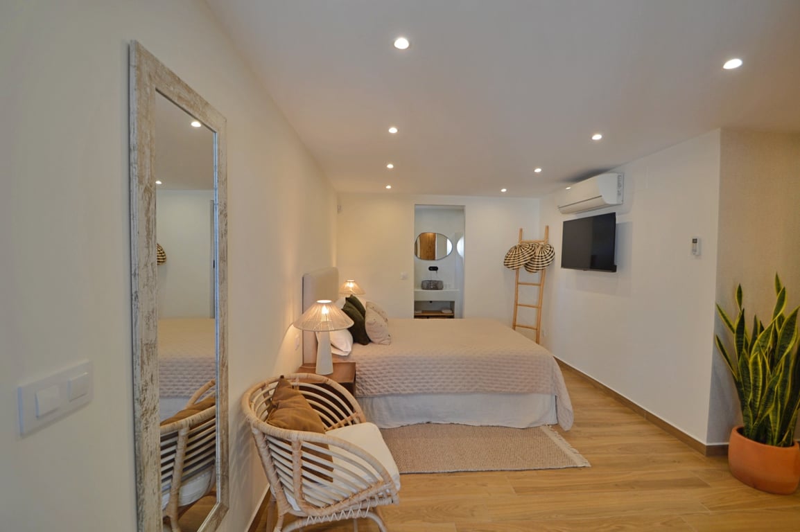 Chambre de style ibizien avec parquet, éclairage LED encastré, climatisation et salle de bain attenante intégrée pour un confort moderne.