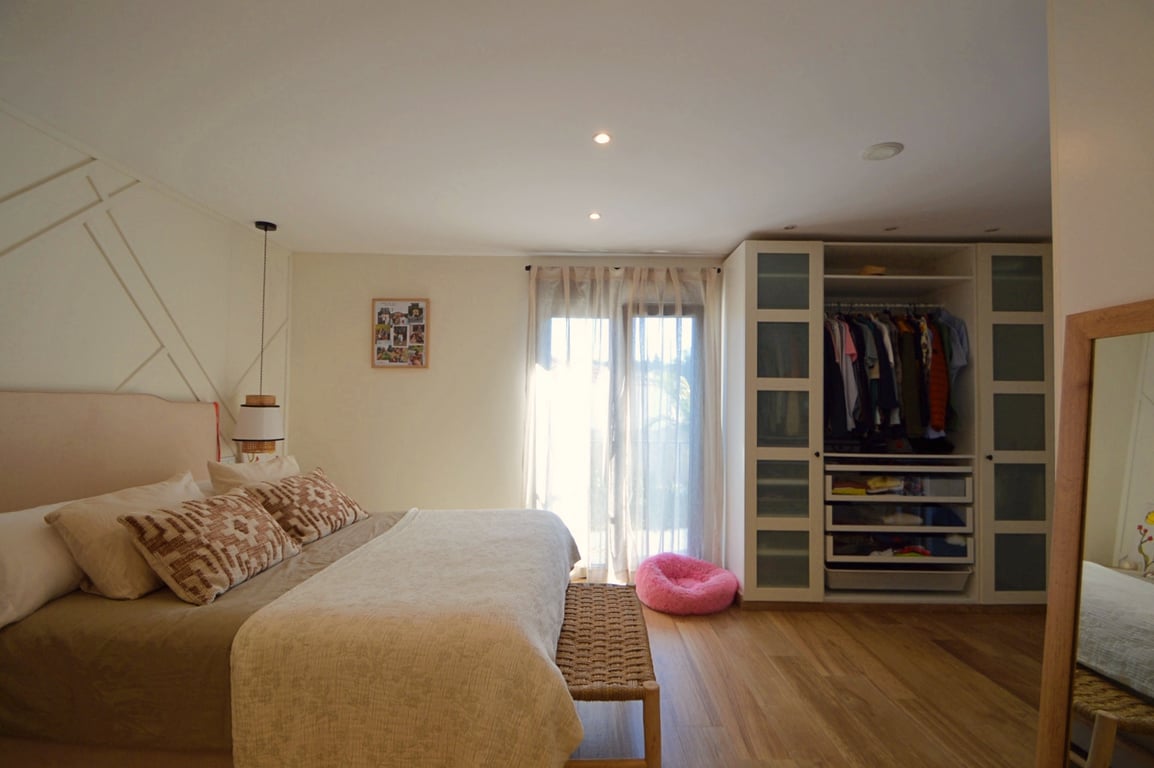 Chambre lumineuse avec parquet en bois clair, mur d'accent géométrique et grand dressing encastré avec portes en verre dépoli et étagères.