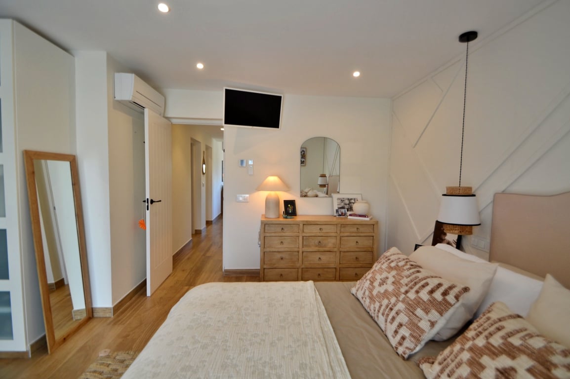 Chambre lumineuse avec parquet, mur décoratif à moulures géométriques, climatisation individuelle et mobilier en bois naturel créant une atmosphère chaleureuse.