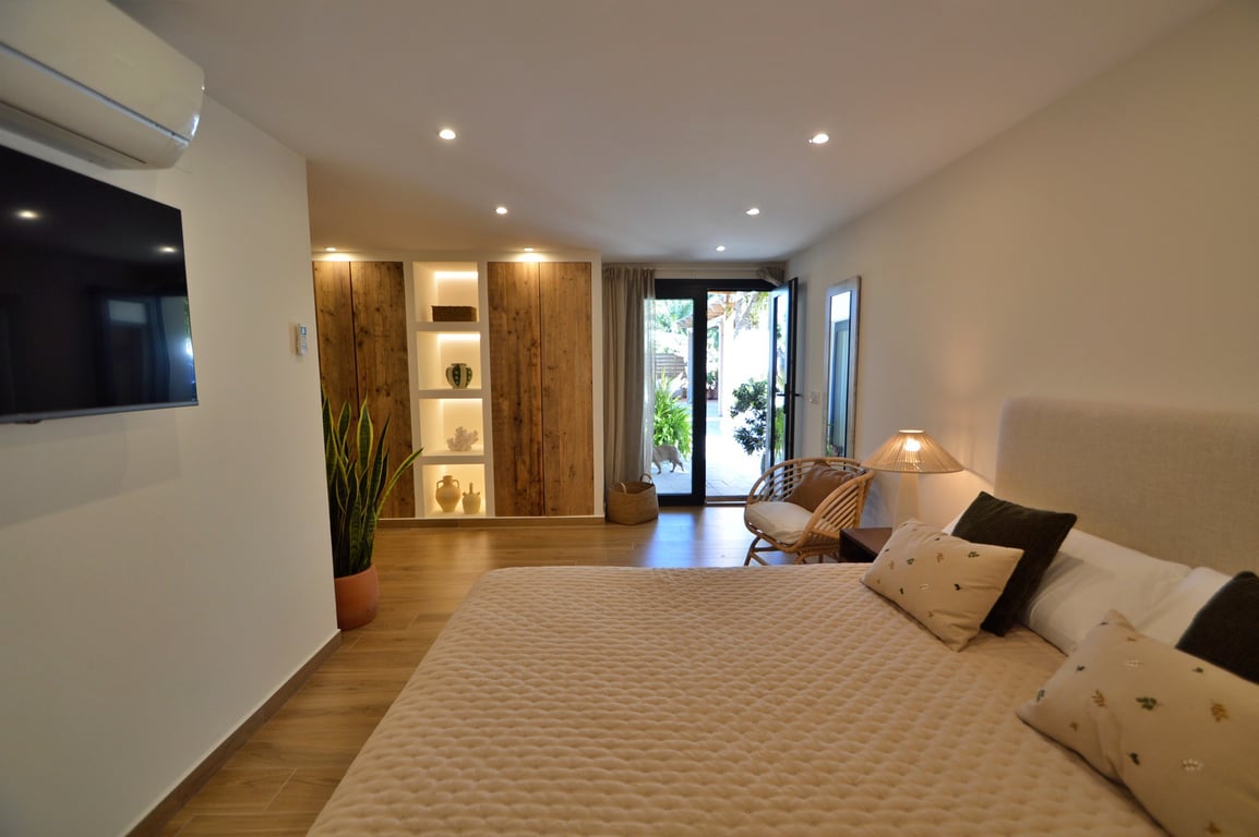 Chambre lumineuse avec placards en bois naturel, étagères rétroéclairées intégrées, sol en grès cérame imitation bois et accès direct à l'extérieur.