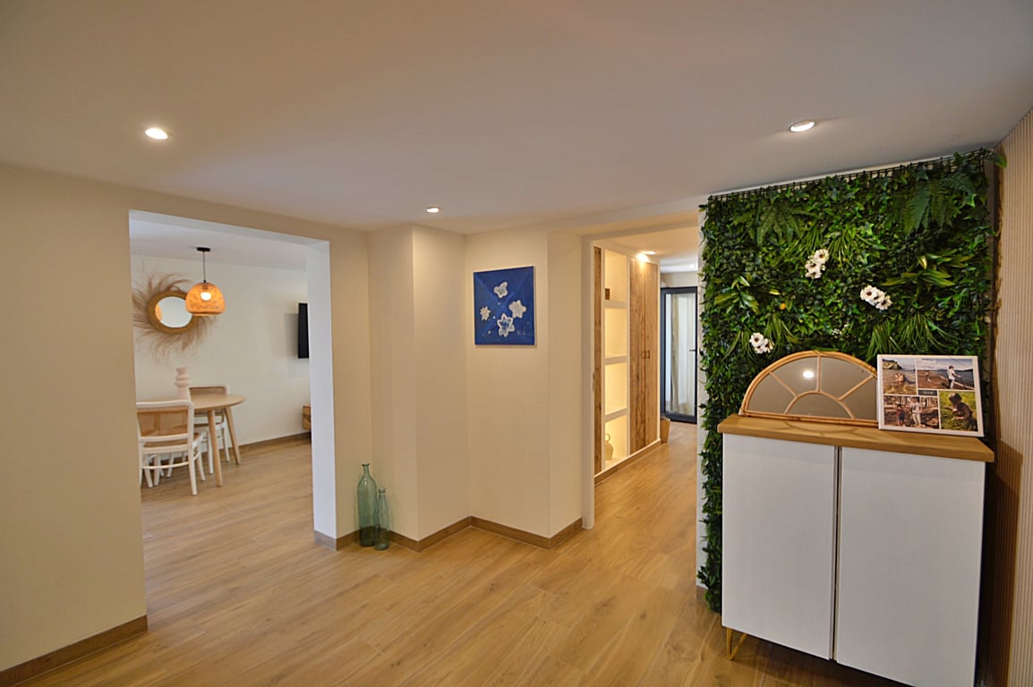 Couloir lumineux avec sol en bois, éclairage encastré et mur végétal décoratif à côté d'un buffet moderne, s'ouvrant sur la salle à manger.