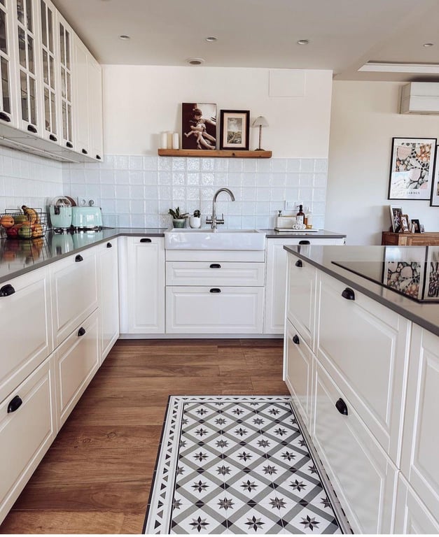 Cuisine moderne de style champêtre avec meubles blancs, plan de travail sombre et évier timbre d'office. Le sol en bois intègre un tapis de carreaux de ciment décoratifs.