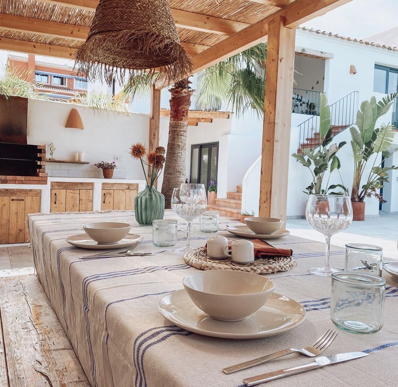 Espace repas extérieur sous une pergola en bois et canisse, comprenant une cuisine d'été avec barbecue intégré et finitions méditerranéennes.