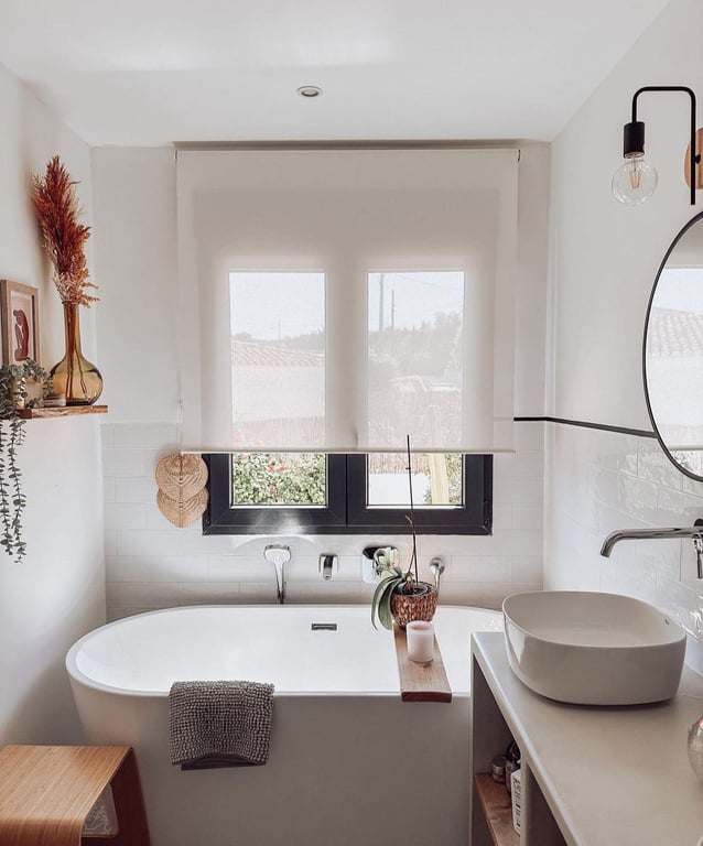 Salle de bain moderne avec baignoire îlot, vasque à poser et fenêtre noire. Le carrelage métro blanc s'harmonise avec des éléments en bois naturel et minimalistes.