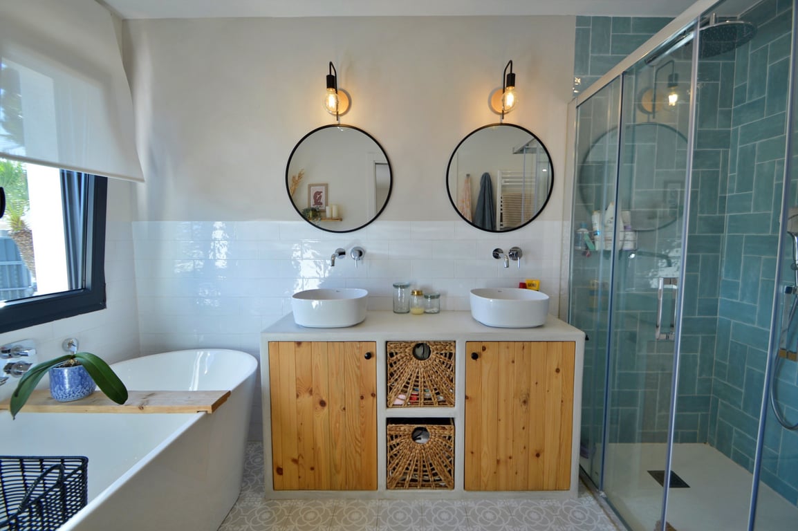 Salle de bain moderne avec double vasque, meubles en bois, baignoire îlot et douche à l'italienne ornée de carreaux turquoise et parois vitrées.