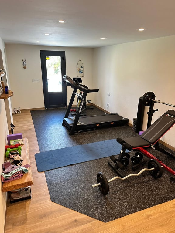 Salle de sport privée équipée d'un tapis de course et de poids, avec sol effet bois, éclairage encastré et accès direct vers l'extérieur.